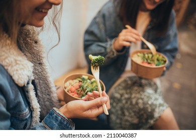 Two Millennial Women Female Friends Sitting Outdoors Eating Takeaway Food, Laughing And Having Fun. Food Delivery And Takeout.