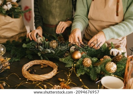 Two millennial women making Christmas wreath using fresh pine branches and festive decorations. Small business