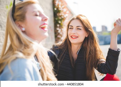 Two Millennials Young Women Blonde And Brunette Friends Outdoor In City Backlight Chatting And Laughing - Focus On Brunette - Friendship, Happiness, Conversation Concept