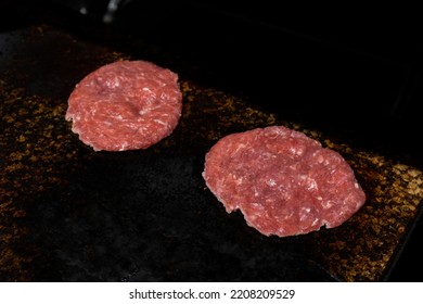 Two Minced Meatballs Are Fried On A Black Surface. The Red Meat Is Not Ready Yet.