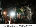 Two miners working in a dimly lit underground tunnel with mining equipment