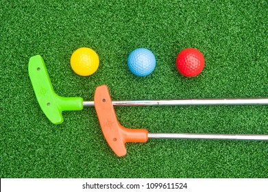 Two Mini Golf Putter With Three Colorful Golf Balls On Synthetic Grass