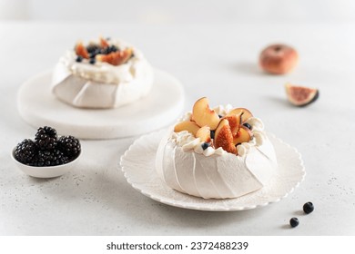 Two mini pavlova cakes from meringue and mascarpone decorated with fresh peach, figs, blackberries and blueberries on a white background. Close up. Confectionery, recipe, menu. Meringue summer dessert