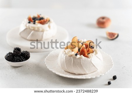 Two mini pavlova cakes from meringue and mascarpone decorated with fresh peach, figs, blackberries and blueberries on a white background. Close up. Confectionery, recipe, menu. Meringue summer dessert