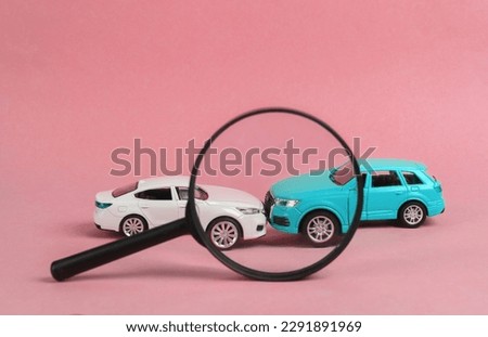 Two mini toy car crash through magnifying glass on pink background, incident, car traffic accident