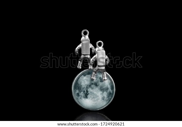 Two miniature\
astronauts floating in space against the Moon\'s face. Close-up\
shot, isolated on black.