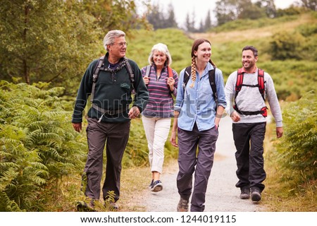 Two mixed age couples walking on a countryside path during family camping adventure, front view