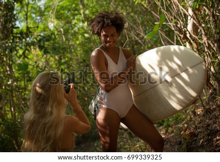 Two mixed race surfer girl bloggers in bikini taking picture on DSLR camera in the jungle