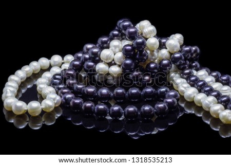 Two mixed strands of natural black pearl beads on a black background