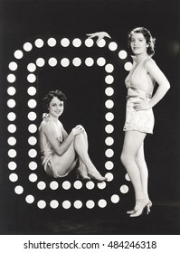Two models posing by large letter O