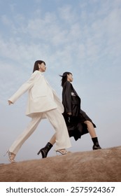 Two Models Strutting Confidently in Chic Outfits Against a Blue Sky Background.