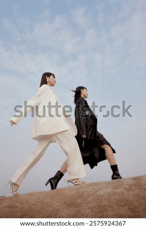 Two Models Strutting Confidently in Chic Outfits Against a Blue Sky Background.