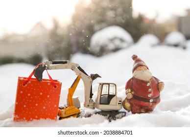 Two models of toy excavators, a souvenir Santa Claus, a gift bag stand in snow. concept for Christmas business greetings, New Year holidays in construction companies. Sunny winter holiday