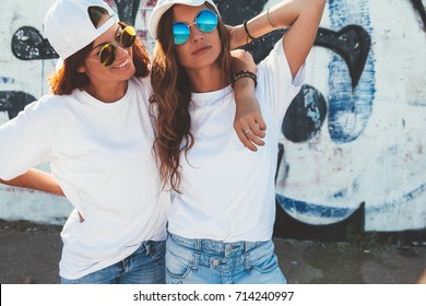 Two Models Wearing Plain White T-shirts And Hipster Sunglasses Posing Against Street Wall. Teen Urban Clothing Style, Same Look. Mockup For Tshirt Print Store. 