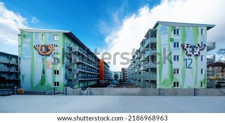 two modern apartment block buildings, artistic designed with a pattern of polygonal shapes, symbolizing floral elements and a painted Checkered butterfly and a large fox butterfly, copy space
