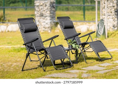 Two modern black zero gravity lounge chairs standing on a green grass lawn in a sunny backyard garden