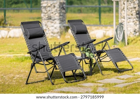 Two modern black zero gravity lounge chairs standing on a green grass lawn in a sunny backyard garden