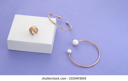 Two modern golden with pearls bracelets and ring on white box on purple background with copy space - Shutterstock ID 2103493043