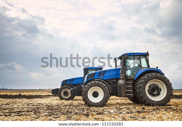 two modern tractors, agricultural machines,\
cultivation of the soil on the farm, a tractor working in a field,\
agricultural machinery in the\
work