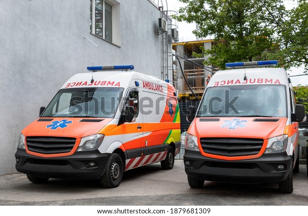 Two modern\
white and orange ambulance medical emergency vans truck parked near\
hospital building. Paramedic vehicles on city street. Healthcare\
and urgent medical support\
concept