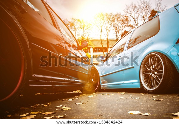 Two modified low cars in brown and\
light blue color. Stance custom cars with a forged polished wheels\
parked on a street at sunny day. Tuned\
automobiles
