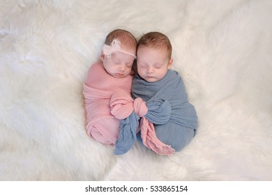 Two month old, boy and girl fraternal twin babies. They are sleeping and swaddled together in pink and blue wraps that are tied together in a bow.