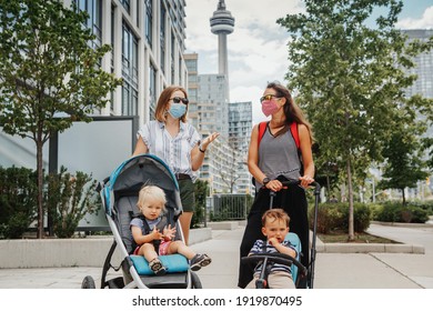 Two Mothers Walking Down The Street With Kids In Strollers. Friends In Face Masks Chatting Talking. People Keeping The Social Physical Distance Outdoor During Covid-19 Coronavirus. New Normal.