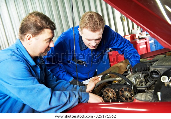 two motor mechanic engineers examining timing\
belt and internal combustion engine of automobile car at repair\
service station