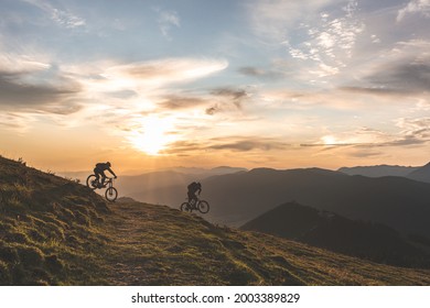 Two mountain bike riders at sunrise ride down a track in the mountains - Powered by Shutterstock