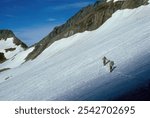 Two mountain climbers are roped together while ascending a snow field on a steep mountainside, on a beautiful day for climbing