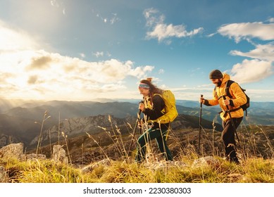 two mountaineers, male and female, trekking up a mountain at sunset. hikers equipped with backpacks, trekking poles and warm clothing walking up the mountain.