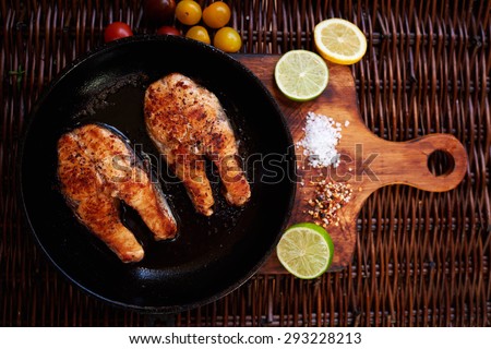 Two mouth-watering deep-fried salmon steak in a frying pan lie expect when the chef starts to serve and serve them to the table, for serving fish, you can use slices of lemon and lime, cherry tomatoes