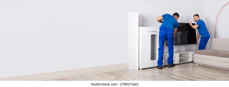 Two Movers Placing Television In Living Room At Home