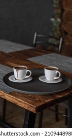 Two Mugs Of Coffee Stands On A Tray In A Restaurant.  Dark Colors, Loft Style Interior.  No People