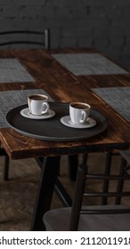 Two Mugs Of Coffee Stands On A Tray In A Restaurant.  Dark Colors, Loft Style Interior.  No People