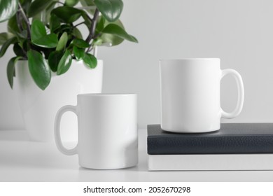 Two mugs mockup with notebook and green plant in pot on white table. front view - Shutterstock ID 2052670298