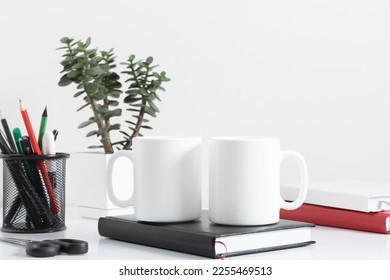 Two mugs mockup with notepad, accessories on white table and green plant in pot. Front view. - Powered by Shutterstock