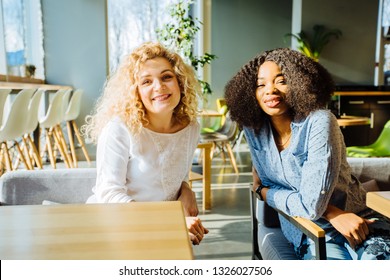 Two Multi Ethnic Friends Enjoying Break Relaxing Together In A Coffee Shop. They Are Sit At A Table Chatting And Laughing.multi-cultural And Difference Of Cultures Strong Friendship Concept.