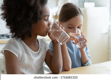 Two multi racial little girls sit at table in kitchen feels thirsty drink clean still natural or mineral water close up image. Healthy life habit of kids, health benefit dehydration prevention concept - Shutterstock ID 1756081310
