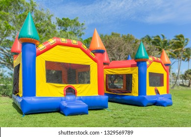 Two multi-color castle bounce houses are ready for the kids.  A beautiful sunny is the perfect time to set up bounce houses at the local park.