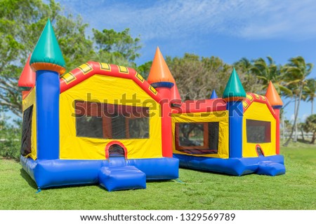 Two multi-color castle bounce houses are ready for the kids.  A beautiful sunny is the perfect time to set up bounce houses at the local park.