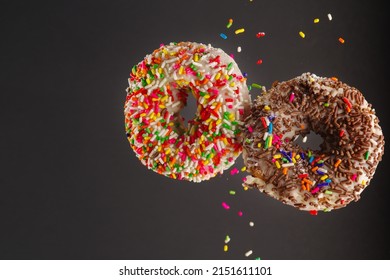 Two Multi-colored Donuts Decorated With Icing Sugar And Confectionery Sprinkles In A Frozen Flight On A Gray Background. Holiday, Birthday. Supermarket, Confectionery. Banner.