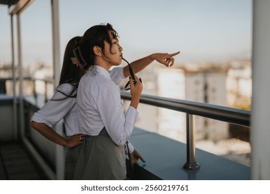 Two multicultural business workers take a break on a rooftop, enjoying the view and engaging in casual conversation, promoting teamwork and relaxation during their workday. - Powered by Shutterstock