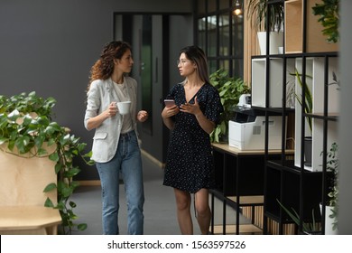 Two multicultural female colleagues enjoying coffee break time, discussing working issues during walk at office. Young vietnamese intern consulting with caucasian female leader at coworking workplace. - Powered by Shutterstock