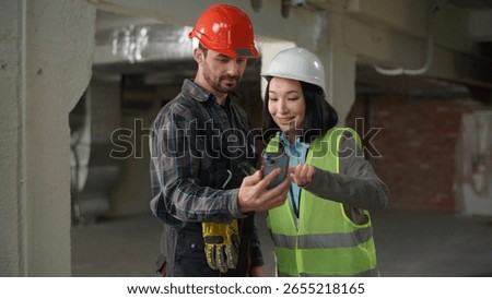 Two multiethnic builders using mobile phone building design app showing thumb up Japanese woman Caucasian man hardhat engineers business inspector browsing smartphone green screen mock up like approve