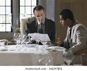 Two multiethnic businessmen sitting at restaurant table and analyzing documents