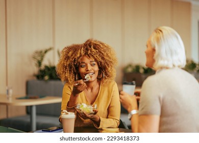 Two multiethnic businesswomen are in the company cafeteria having a casual lunch and chatting. - Powered by Shutterstock