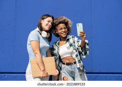 two multiethnic friends taking pictures with cell phones, with headphones and laptop, on a nice blue wall - Shutterstock ID 2021889533