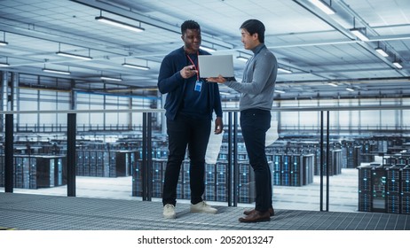 Two Multiethnic Male Data Center System Administrators and IT Specialists Talk, Use Laptop. Information Technology Engineers work on Cyber Security Network Protection in Cloud Computing Server Farm. - Powered by Shutterstock