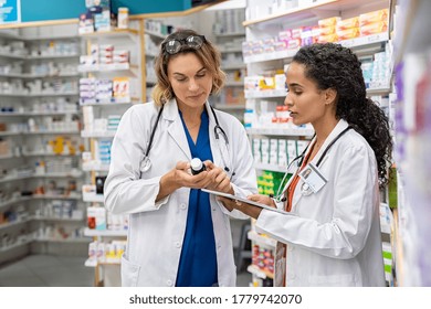 Two Multiethnic Pharmacists Checking Inventory At Hospital Pharmacy. Medical Staff Working In Drugstore. Mature Woman Pharmacist With African Colleague Holding Cough Syrup And Medicines.